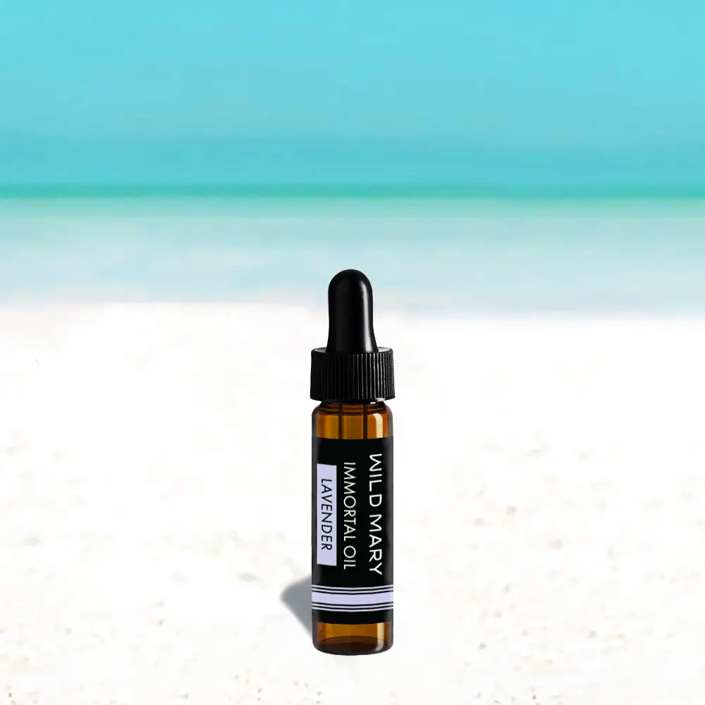 Wild Mary Immortal Oil — Lavender Mini, 0.25 oz face oil bottle on a beach background with white sand and light blue sky.