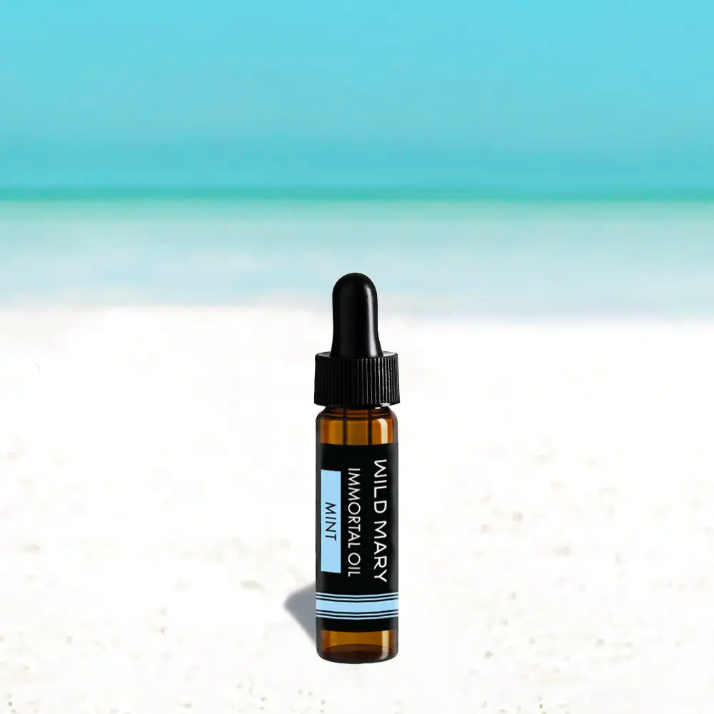 Wild Mary Immortal Oil — Mint Mini, 0.25 oz face oil bottle on a beach background with white sand and light blue sky.