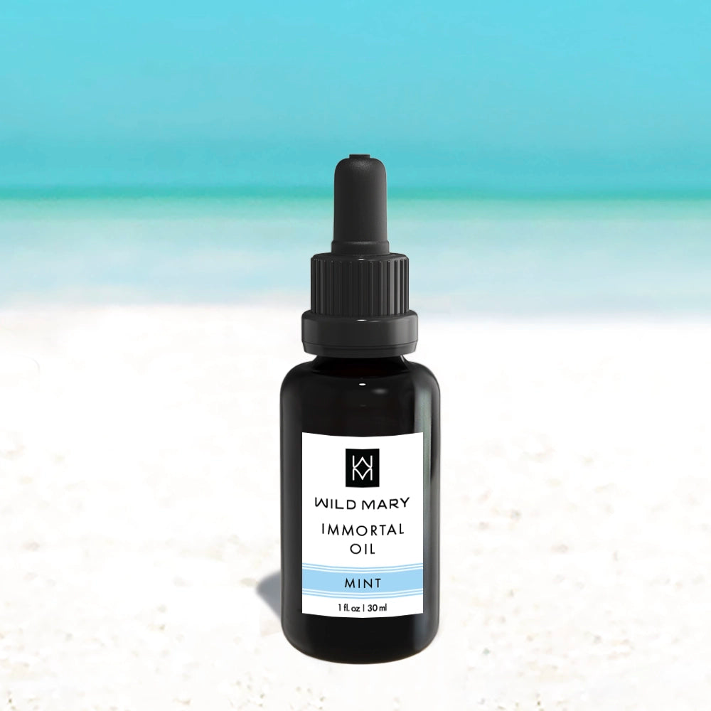 Wild Mary Immortal Oil — Mint variant, 1 oz face oil bottle on a beach background with white sand and light blue sky.