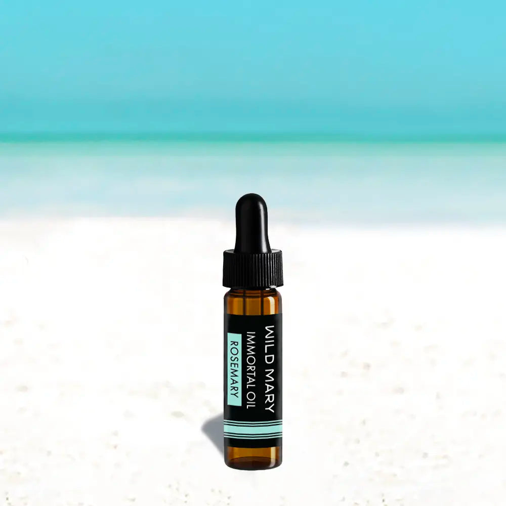 Wild Mary Immortal Oil — Rosemary Mini, 0.25 fl oz face oil bottle on a beach background with white sand and light blue sky.