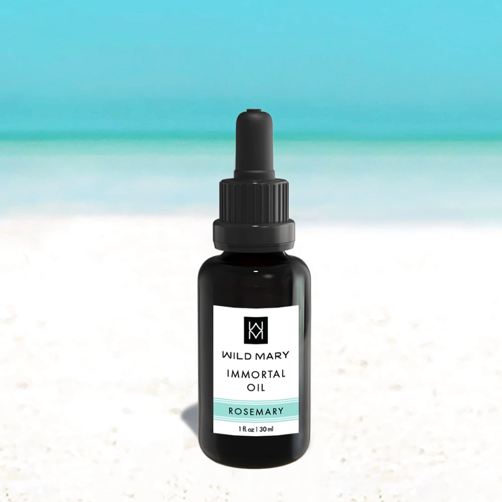 Wild Mary Immortal Oil — Rosemary variant, 1 oz face oil bottle on a beach background with white sand and light blue sky.