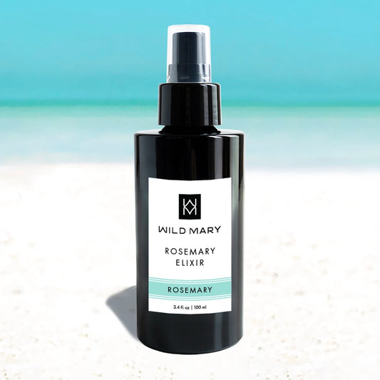 Wild Mary Rosemary Elixir — Rosemary variant, 3.4 oz bottle on a beach background with white sand and light blue sky. 