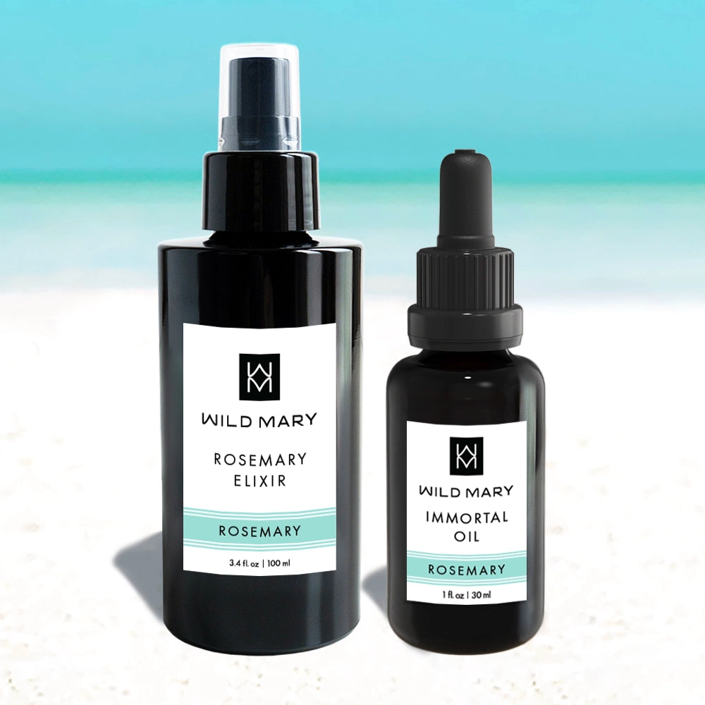 Wild Mary Rosemary Elixir and Immortal Oil skincare bottles on a beach background with light blue and white gradient.